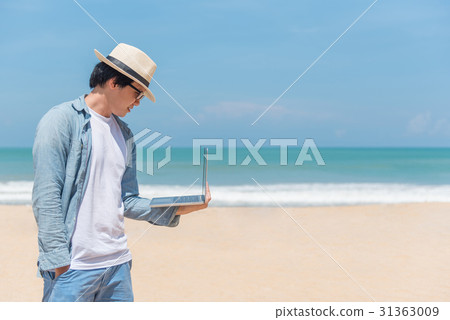 Young Asian man holding laptop on the beach Young Asian man holding laptop on the beach 31363009