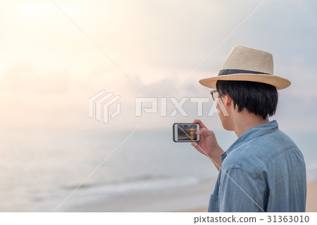 young man taking photos on the beach by smartphone young man taking photos on the beach by smartphone 31363010