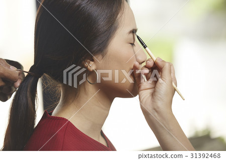 a girl is getting eyebrows make-up and hair style. 31392468