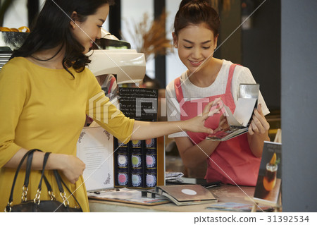 a woman is choosing beverage in bar counter with a waitress. a woman is choosing beverage in bar counter with a waitress. 31392534