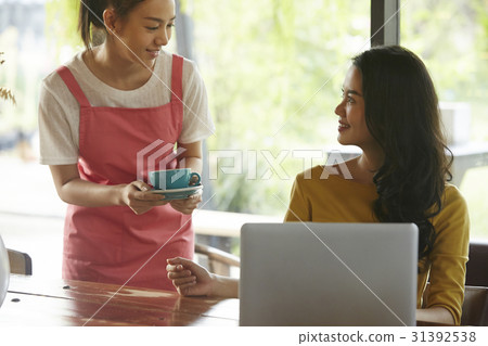 a waitress is bringing a cup of coffee to a happy woman. a waitress is bringing a cup of coffee to a happy woman. 31392538
