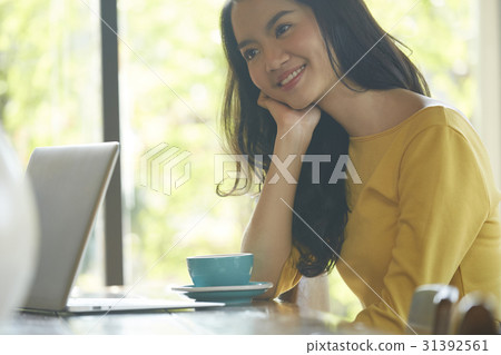 a woman is sitting and smiling beside a cup of coffee, laptop. a woman is sitting and smiling beside a cup of coffee, laptop. 31392561