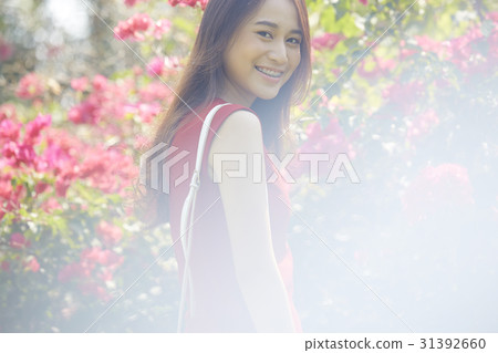 Beautiful girl in a red dress is smiling in a flower garden. 31392660