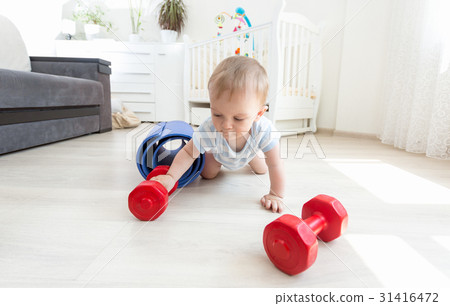 Baby exercising with dumbbells on floor at home Baby exercising with dumbbells on floor at home 31416472