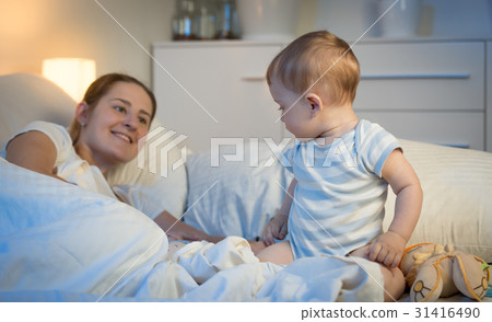 Baby sitting on bed at night and looking at mother 31416490