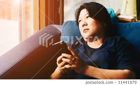 Asia women 40s holding smartphone thinking on sofa 31441979