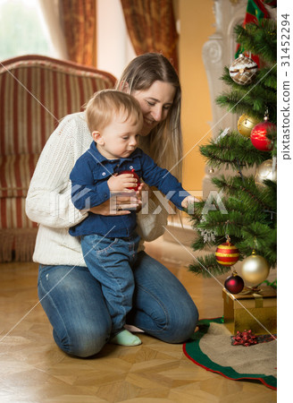 Mother showing baby how to decorate Christmas tree Mother showing baby how to decorate Christmas tree 31452294