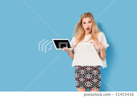 Young woman on blue background points her tablet 31453416