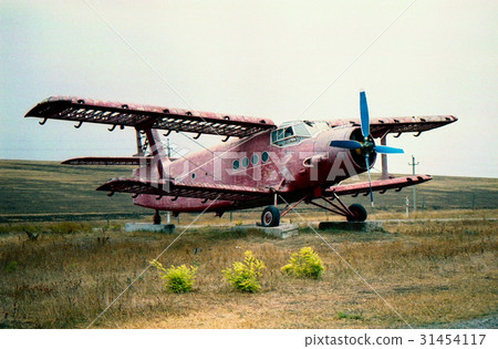 An old, abandoned, red plane stands in the field 31454117
