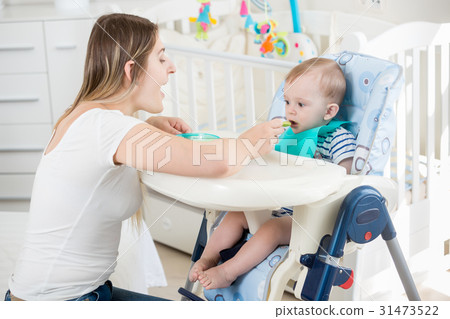 woman feeding her baby in highchair at living room 31473522