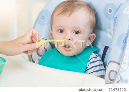 baby in apron eating fruit sauce from spoon baby in apron eating fruit sauce from spoon 31473523