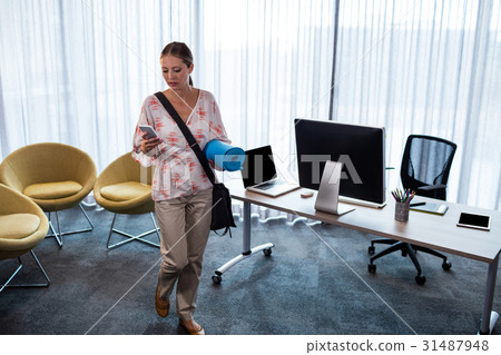 Businesswoman holding an exercise mat and looking her mobile phone Businesswoman holding an exercise mat and looking her mobile phone 31487948