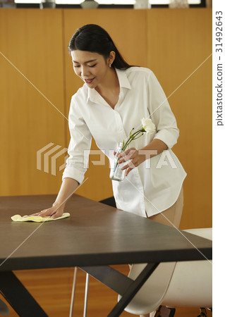 a maid is cleaning the table and holding a flower vase. 31492643
