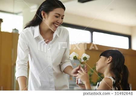 mom is smiling when giving a flower vase to daughter. 31492648