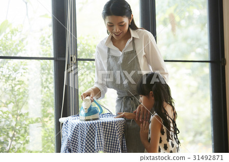A little daughter wants help her mother ironing clothes. A little daughter wants help her mother ironing clothes. 31492871