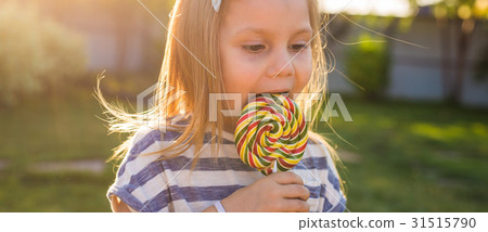 cute little girl eating a lollipop on the grass in cute little girl eating a lollipop on the grass in 31515790