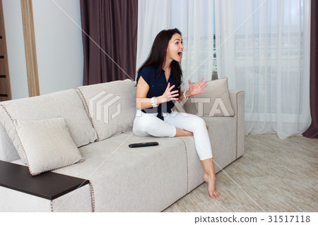 Woman watching tv at home and holding a remote Woman watching tv at home and holding a remote 31517118