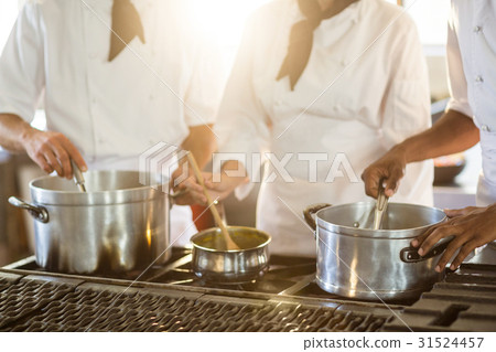 Mid section of chefs stirring in cooking pot Mid section of chefs stirring in cooking pot 31524457
