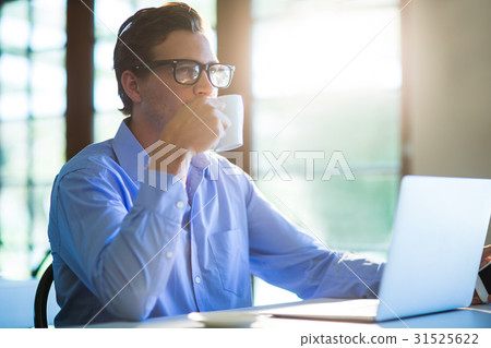 Man drinking a coffee while using a laptop Man drinking a coffee while using a laptop 31525622