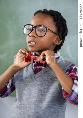 Thoughtful schoolboy adjusting a bow tie in classroom Thoughtful schoolboy adjusting a bow tie in classroom 31526827