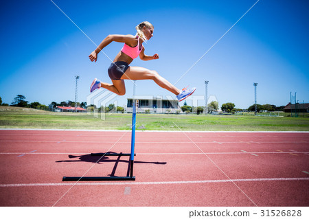 Female athlete jumping above the hurdle Female athlete jumping above the hurdle 31526828