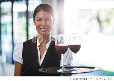 Smiling waitress holding a tray with glasses of red wine 31527955
