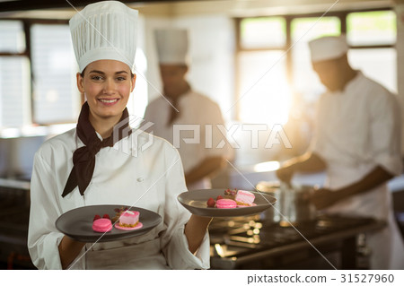 Portrait of smiling female chef presenting dessert plates Portrait of smiling female chef presenting dessert plates 31527960