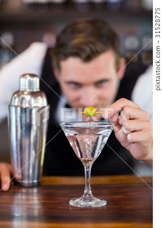 Bartender garnishing cocktail with olive 31528775