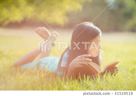 Thoughtful girl lying on grass and reading book in park Thoughtful girl lying on grass and reading book in park 31529519