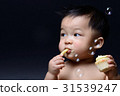 Cute asian baby boy is eating french fries and cake with both hi 31539247