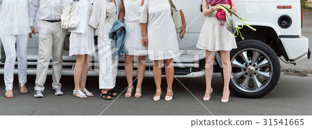People dressed in white posing next to limousine 31541665