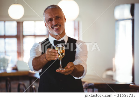 Smiling bartender offering a glass of wine at bar counter 31555733