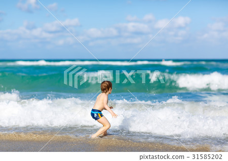 little blond kid boy having fun on ocean beach in 31585202