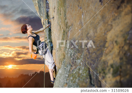 Female climber climbing with rope on a rocky wall 31589026