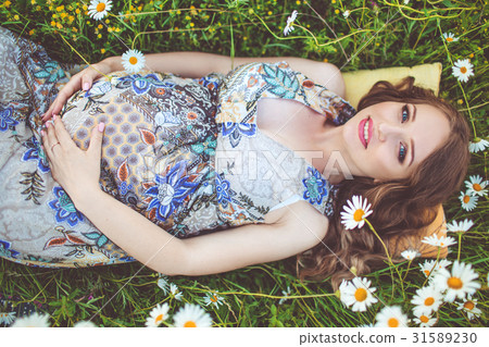Beautiful pregnant woman lying in the camomile Beautiful pregnant woman lying in the camomile 31589230