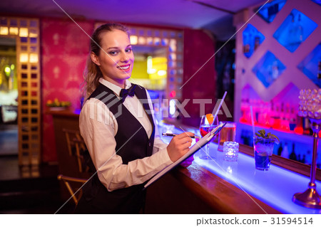 Barmaid writing in clipboard at illuminated bar counter 31594514