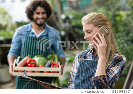Female gardener talking on cellphone while man in background Female gardener talking on cellphone while man in background 31594527