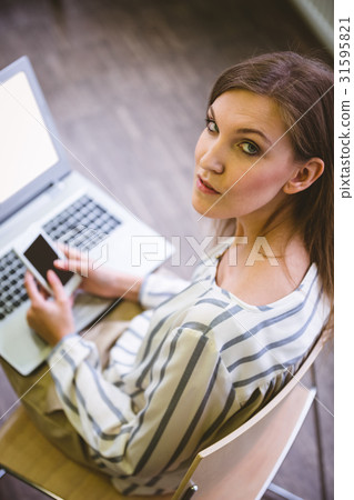 Portrait of confident businesswoman using cellphone over laptop at office 31595821