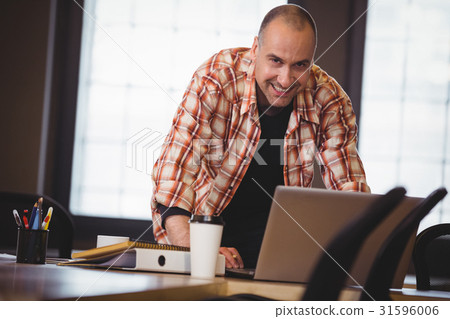 Businessman leaning while using laptop at desk in creative office 31596006