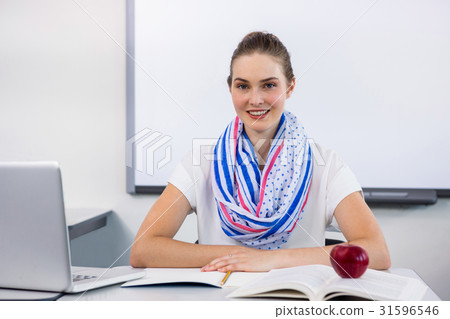 Portrait of smiling teacher sitting at desk in... - Stock Photo ...