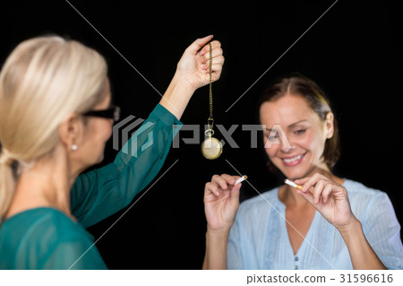 Hypnotherapist holding pendulum by patient 31596616
