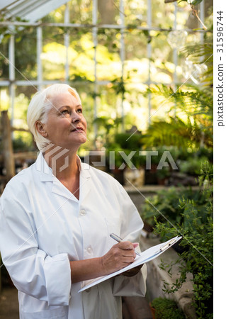Female scientist writing in clipboard while examining plants 31596744