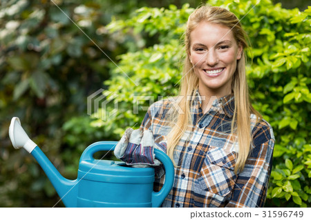 Confident female gardener holding watering can Confident female gardener holding watering can 31596749
