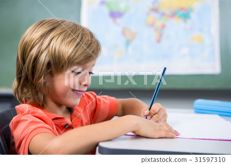Smiling boy writing on book in classroom 31597310