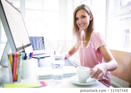 Female graphic designer having coffee at desk Female graphic designer having coffee at desk 31597348