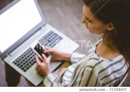 High angle view of businesswoman using cellphone over laptop at office High angle view of businesswoman using cellphone over laptop at office 31598047
