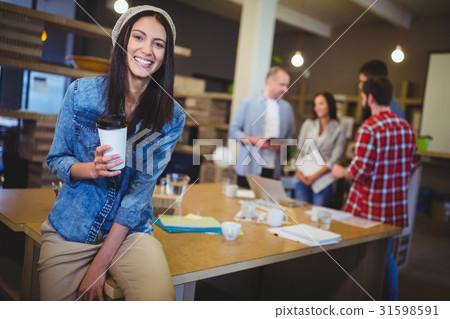 Happy businesswoman holding disposable cup in office 31598591