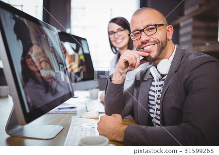 Confident businessman by computer with colleague in background 31599268