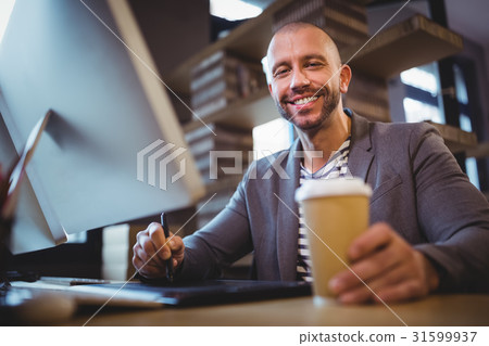 Creative businessman holding disposable cup while using graphics tablet Creative businessman holding disposable cup while using graphics tablet 31599937