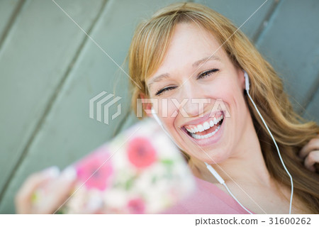 Young Adult Woman Wearing Earphones Taking a Selfie with Her Sma 31600262